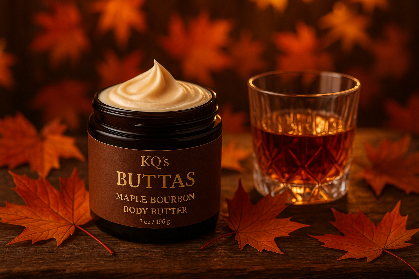 KQ's BUTTAs Maple bourbon body butter in an open jar make a fall background with maple leaves and a glass of bourbon